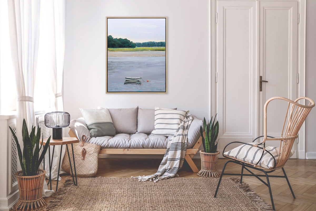 A limited edition landscape print framed in a light wood frame hangs on a white wall above a loveseat sofa and armchair, with potted plants and a woven carpet. 