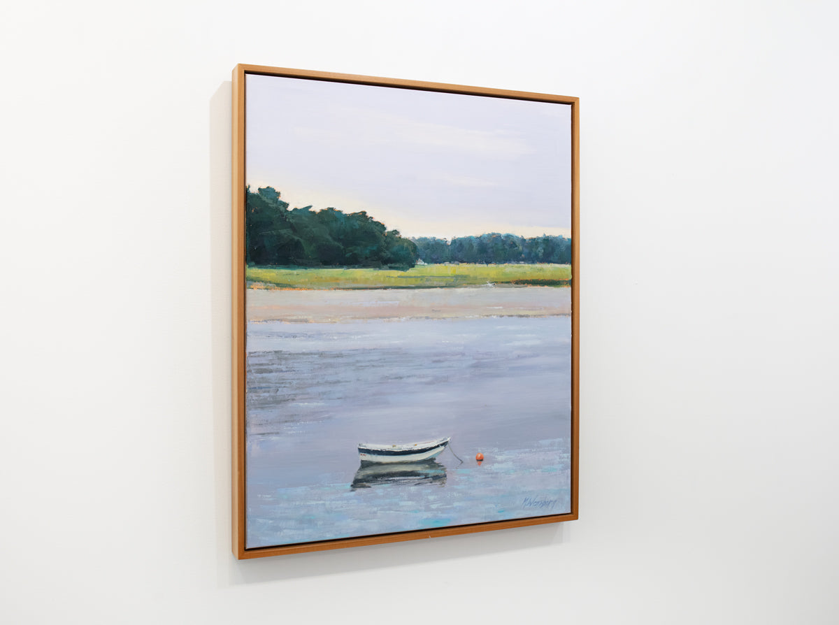 A light coastal landscape painting framed in a light wood frame hangs on a white wall.