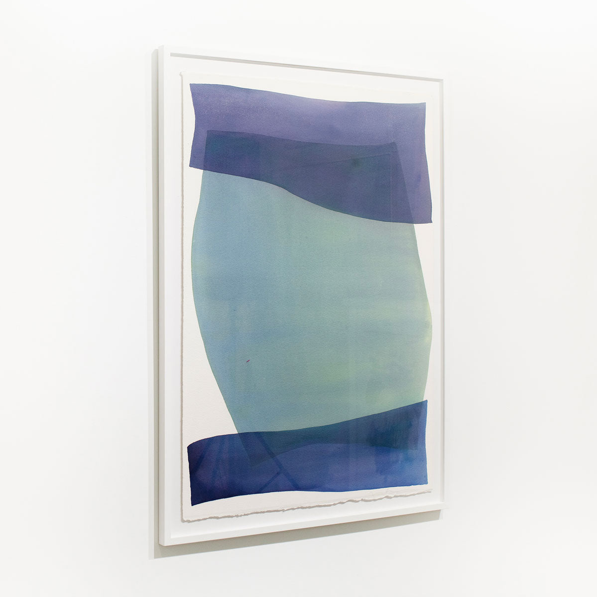 A green and blue abstract watercolor painting framed in a white frame hangs on a white wall.