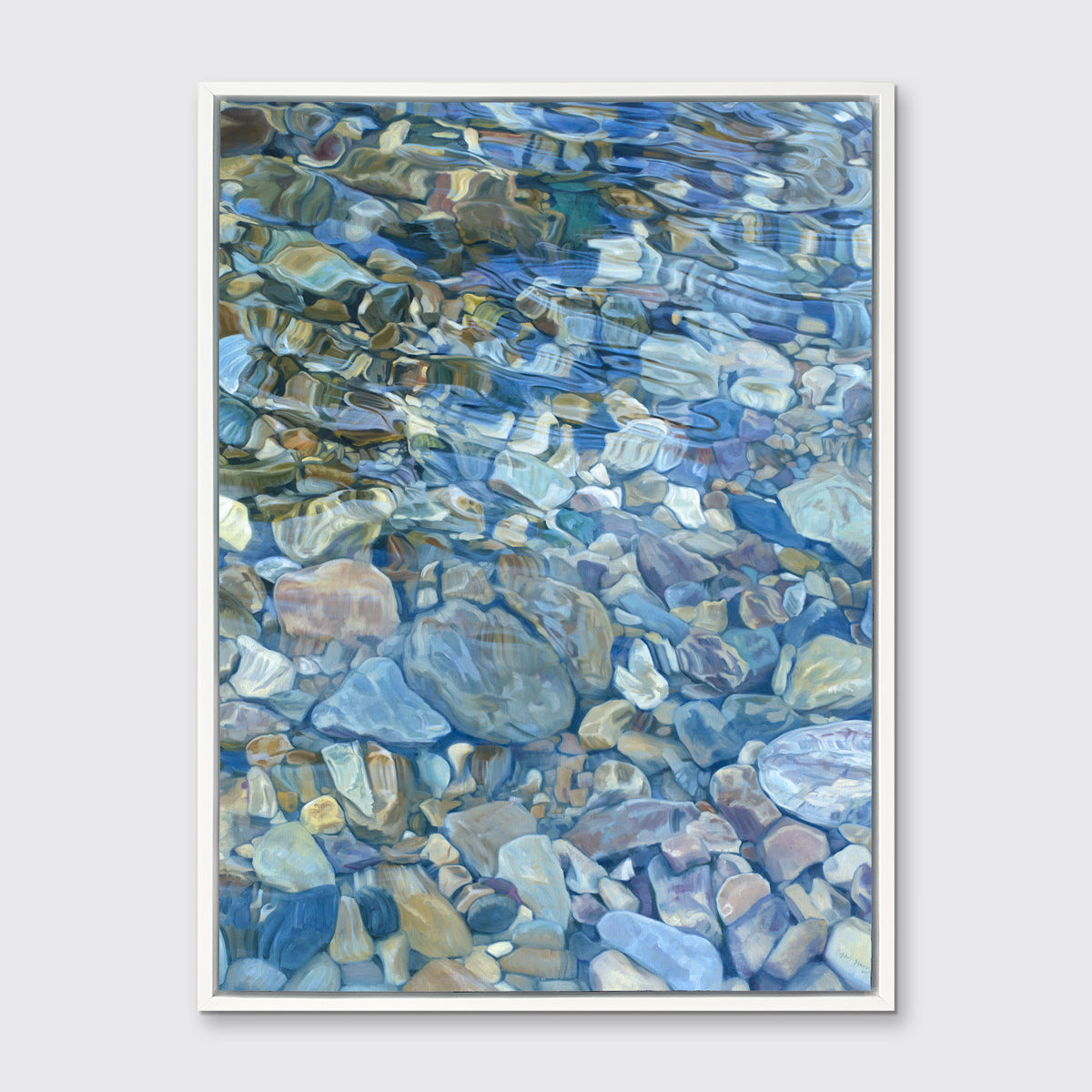 Abstracted river rocks under water hangs in a white floater frame on a light grey wall.