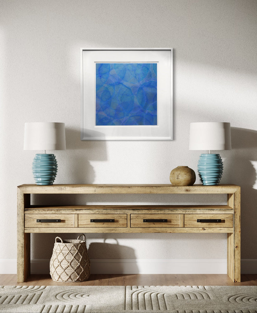 Wooden console table with two lamps and a framed blue artwork on a white wall.