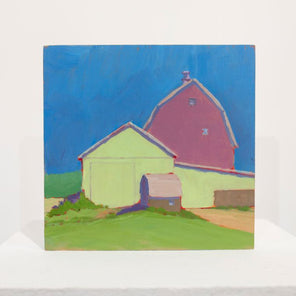 A blue, pink, and green contemporary landscape painting sits upright on a white table surface in front of a white wall. 