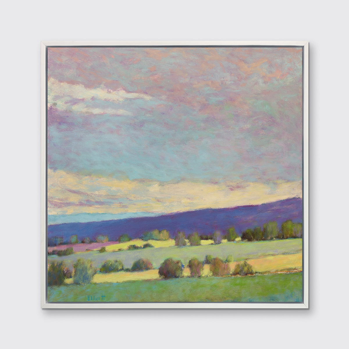 A blue, green and purple abstract landscape print in a white floater frame hangs on a white wall.