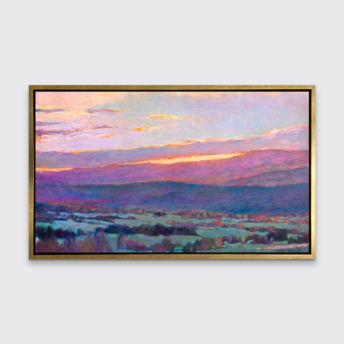 A pink, blue and green abstract landscape print in a gold floater frame hangs on a white wall.