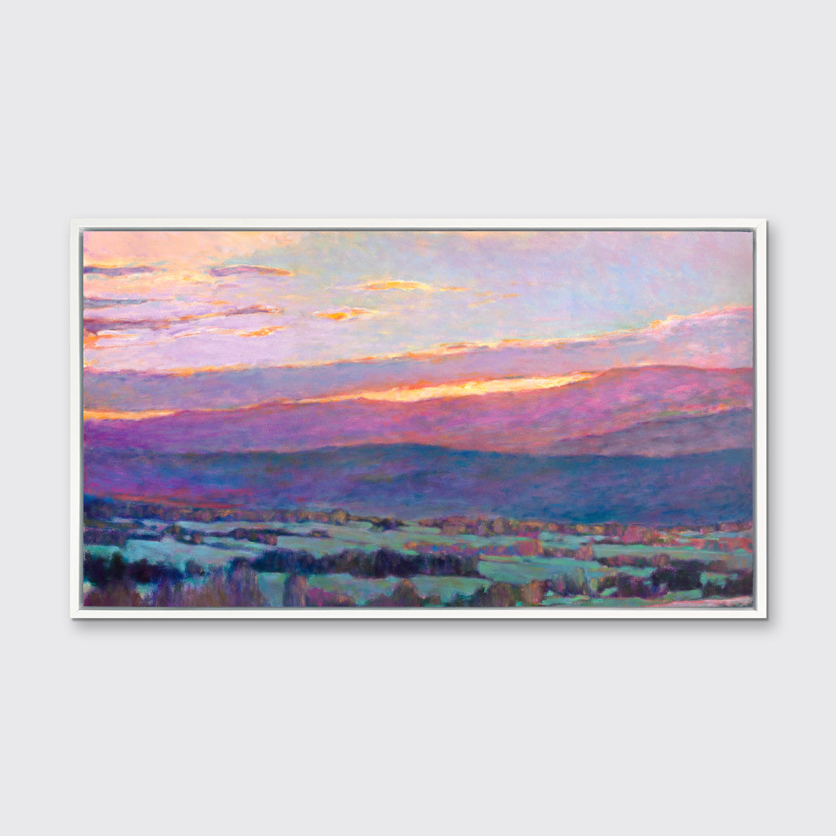 A pink, blue and green abstract landscape print in a white floater frame hangs on a white wall.