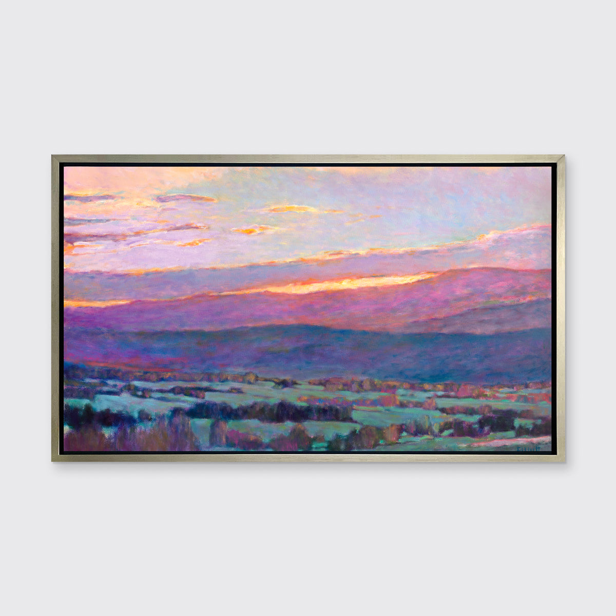 A pink, blue and green abstract landscape print in a silver floater frame hangs on a white wall.
