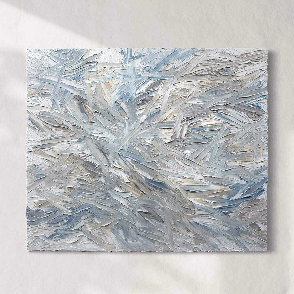 An original abstract painting heavily textured with blue and gray tones on a white wall