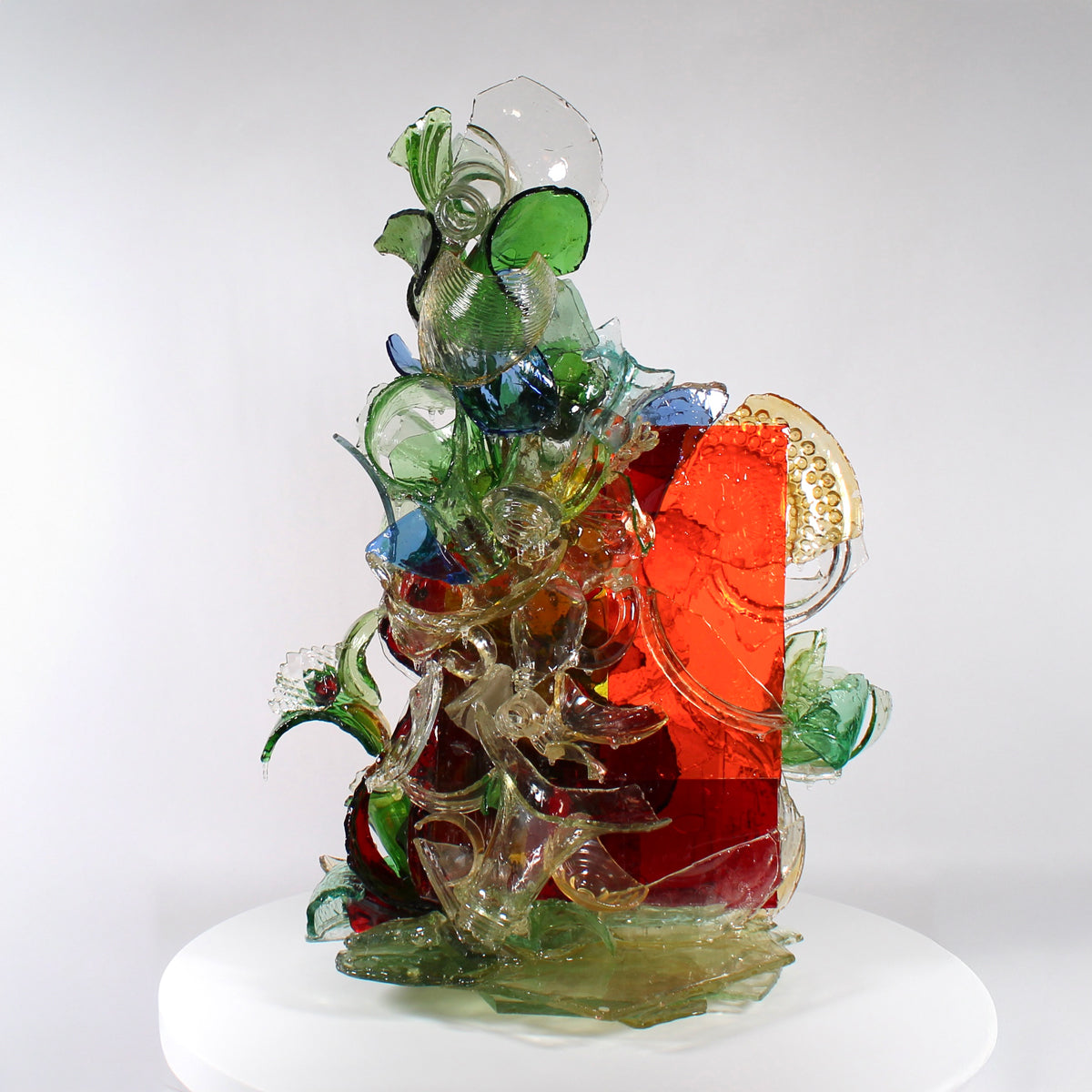 Colorful glass sculpture on a white pedestal with a white background.