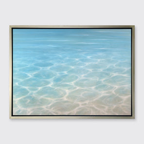 A tonal teal, beige and white abstract seascape print in a silver floater frame hangs on a white wall.