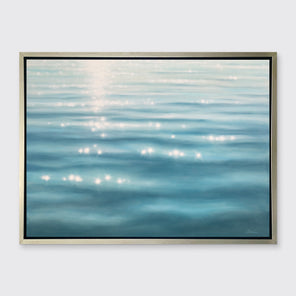 A tonal blue and white seascape print in a silver floater frame hangs on a white wall.