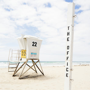 A coastal photograph of a lifeguard stand by Peter Mendelson with a sign in the foreground that says "The Office."