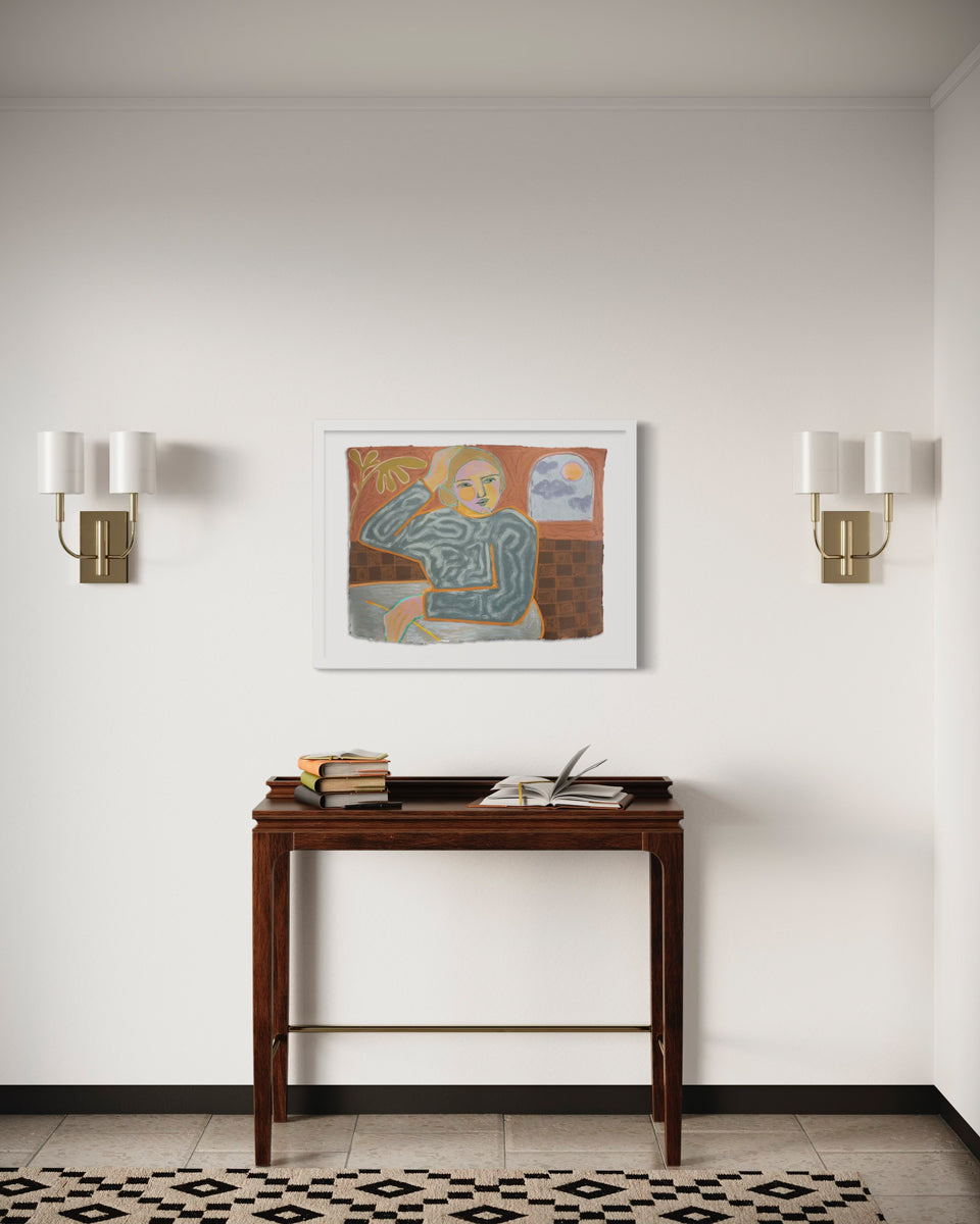 A framed yellow, orange, and grey abstracted figure painting hangs on a white wall between two modern sconces and above a wooden console table and brown and black carpet. 