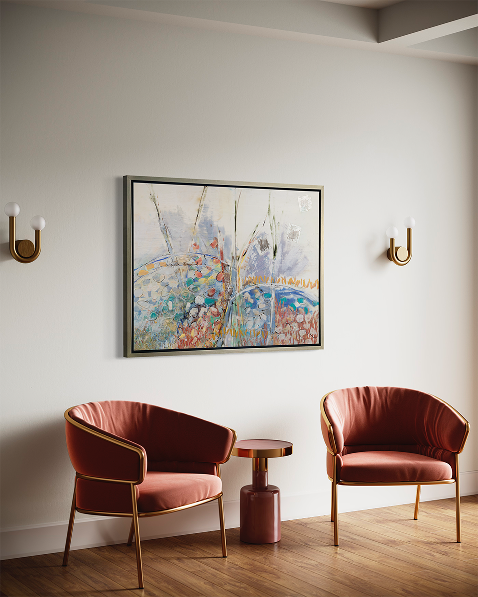 A side view of a multicolored abstract floral print in a silver floater frame hangs on a white wall above two rust red chairs and a round pedestal table.