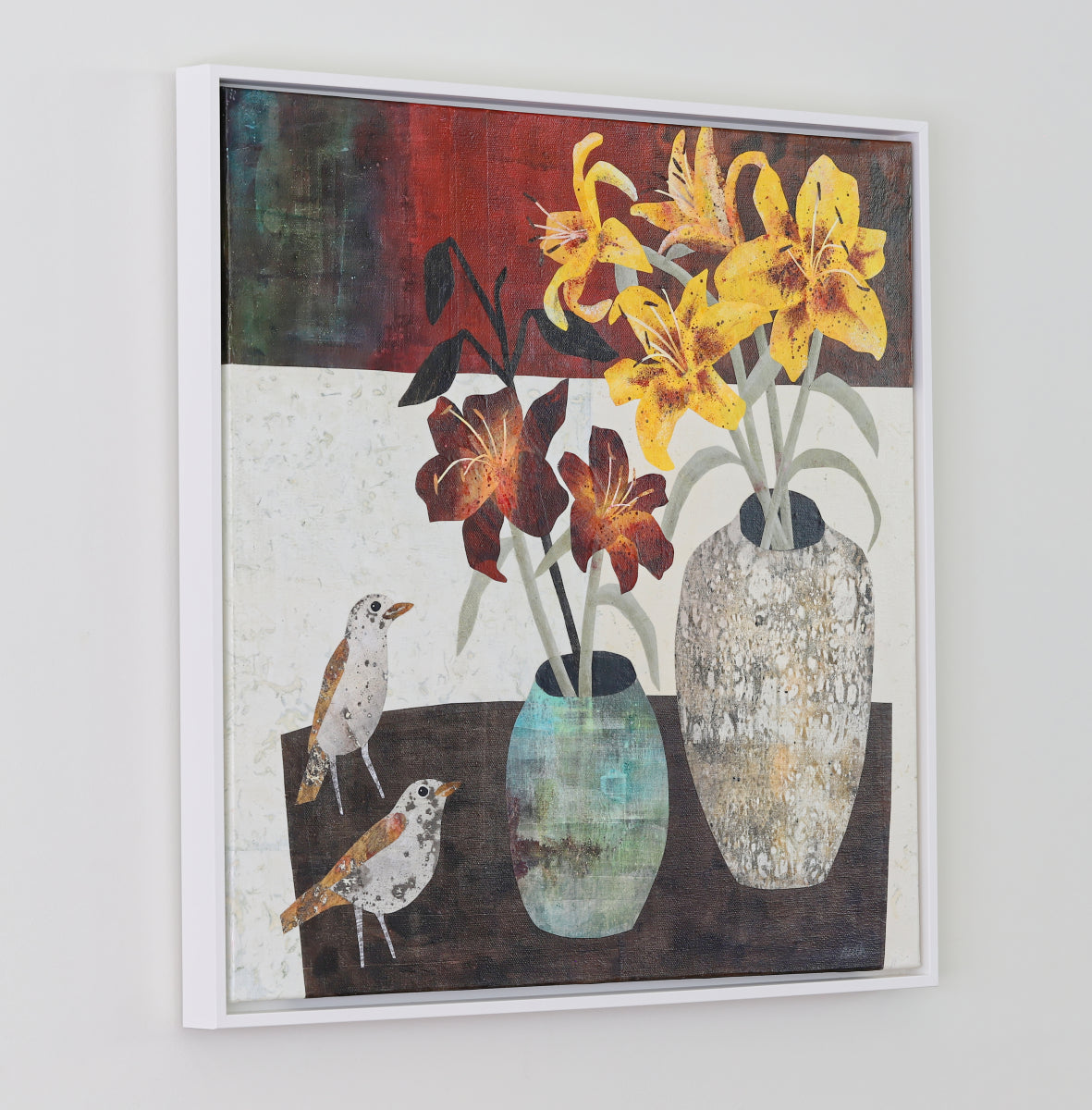 A framed still life collage painting featuring yellow and burgundy lilies in textured ceramic vases, with two small birds on the left, shown hanging on a light gray wall.