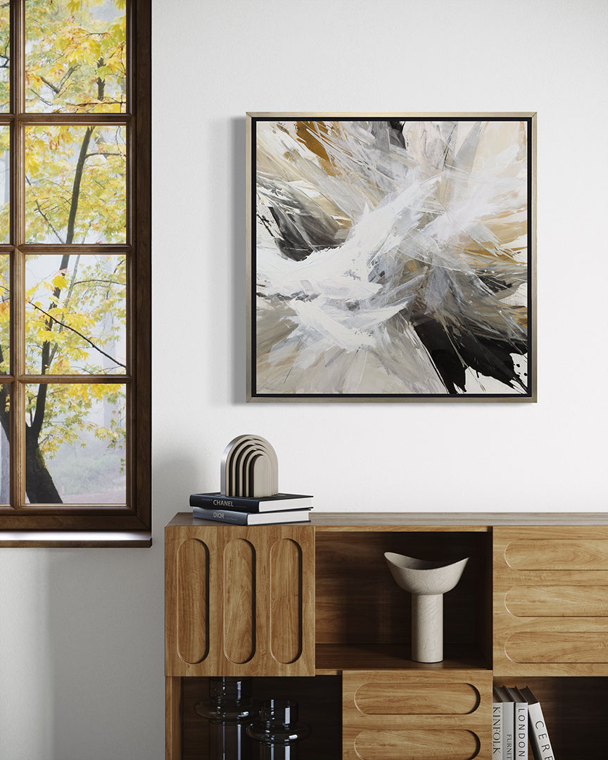 A white, umber, black, grey, yellow ocher and gold abstract print in a silver floater frame hanging on a wall over a Yellow Ocher chair and a Credenza with a window to the left.