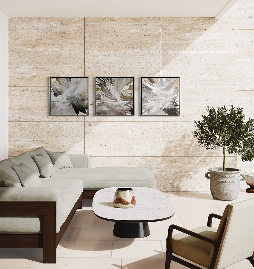 3 white, umber, black, grey, yellow ocher and gold abstract print in a silver floater frame hanging on a wall over a Yellow Ocher chair and a coffee table with white ceramic pots.