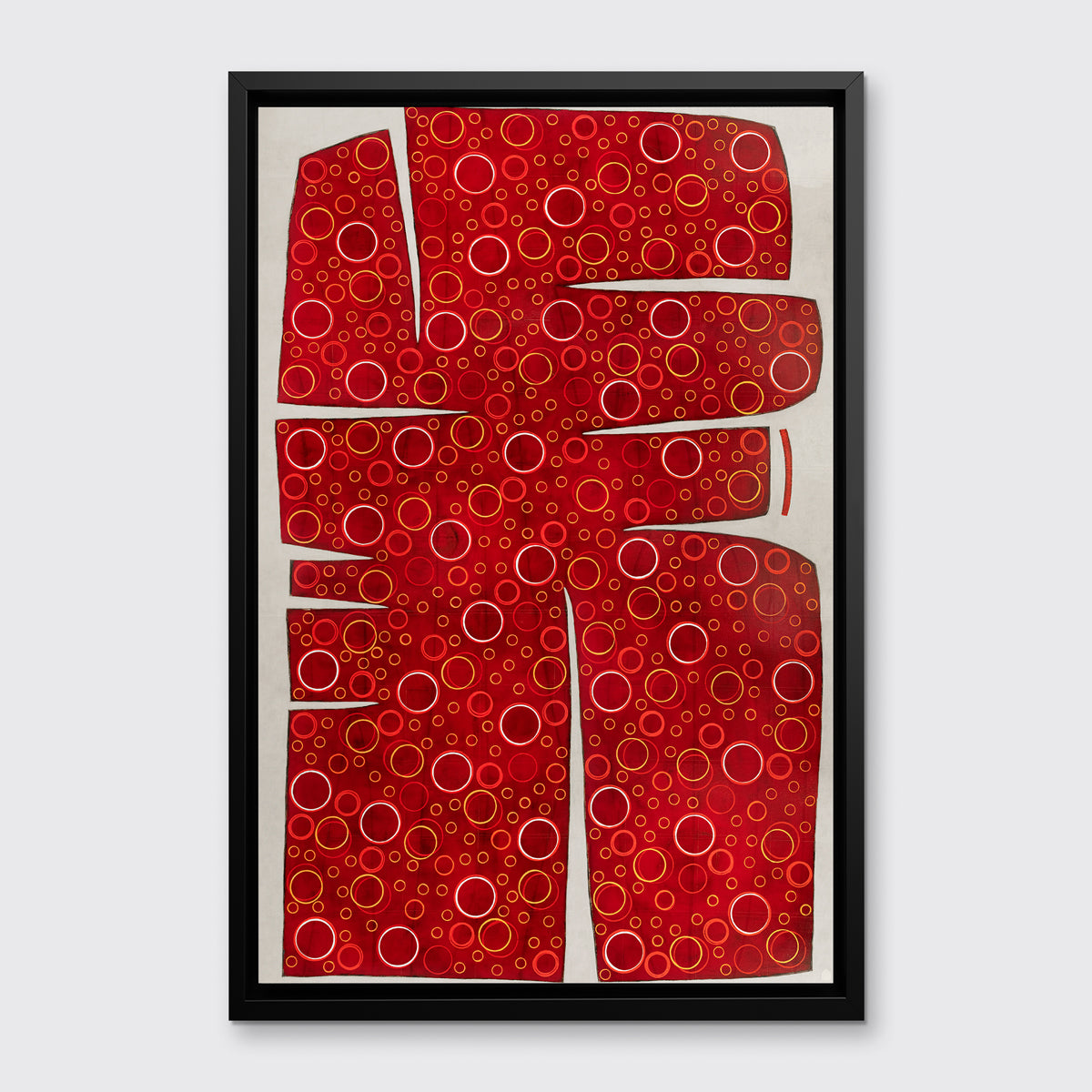 A red, yellow and white abstract print in a black floater frame hangs on a white wall.