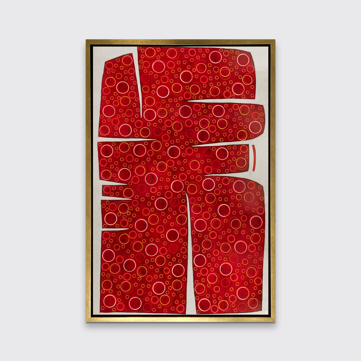 A red, yellow and white abstract print in a gold floater frame hangs on a white wall.