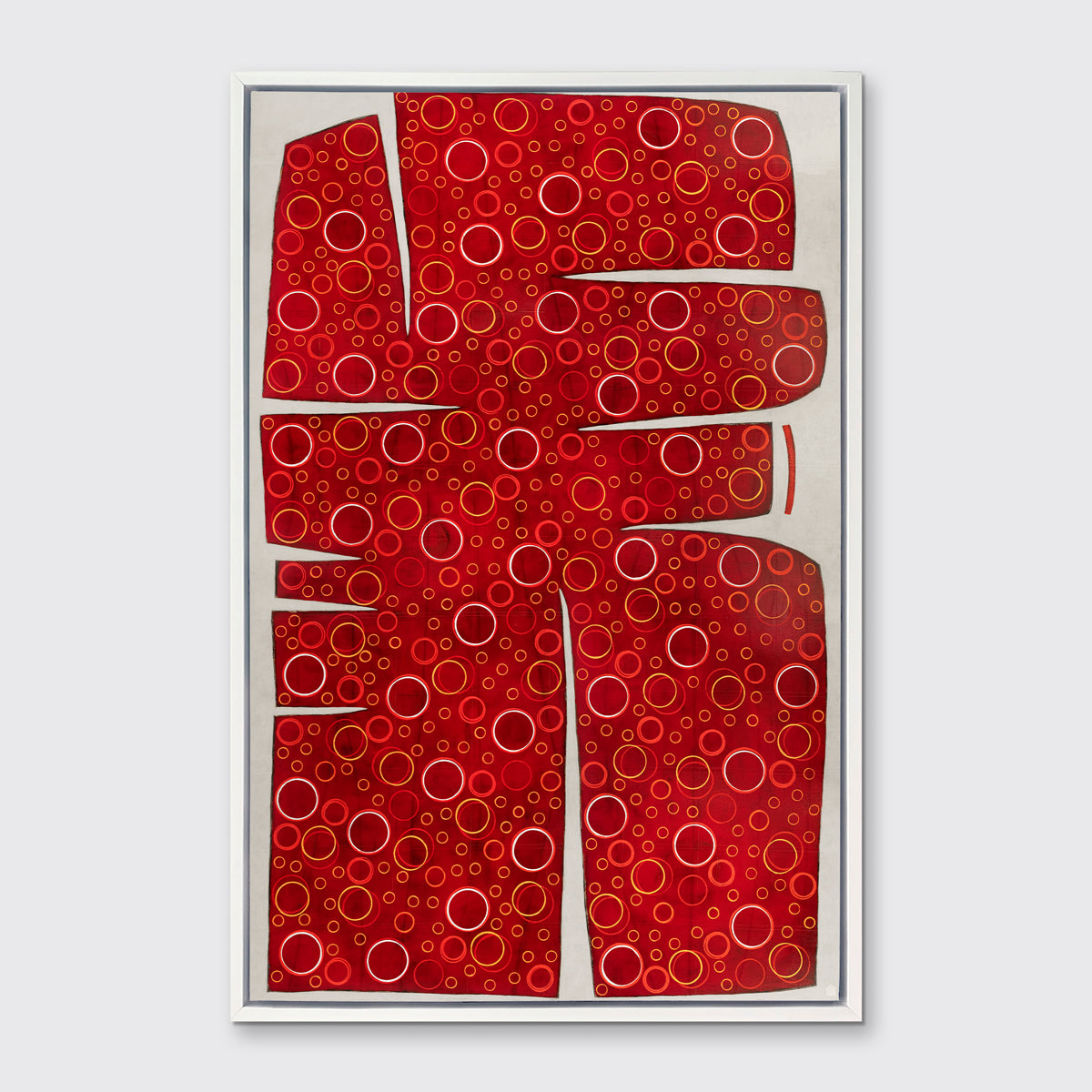 A red, yellow and white abstract print in a white floater frame hangs on a white wall.