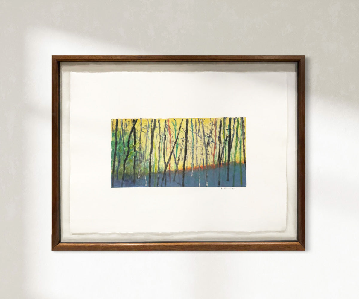 Framed artwork of a forest scene with trees in yellow and green hanging on a white wall.
