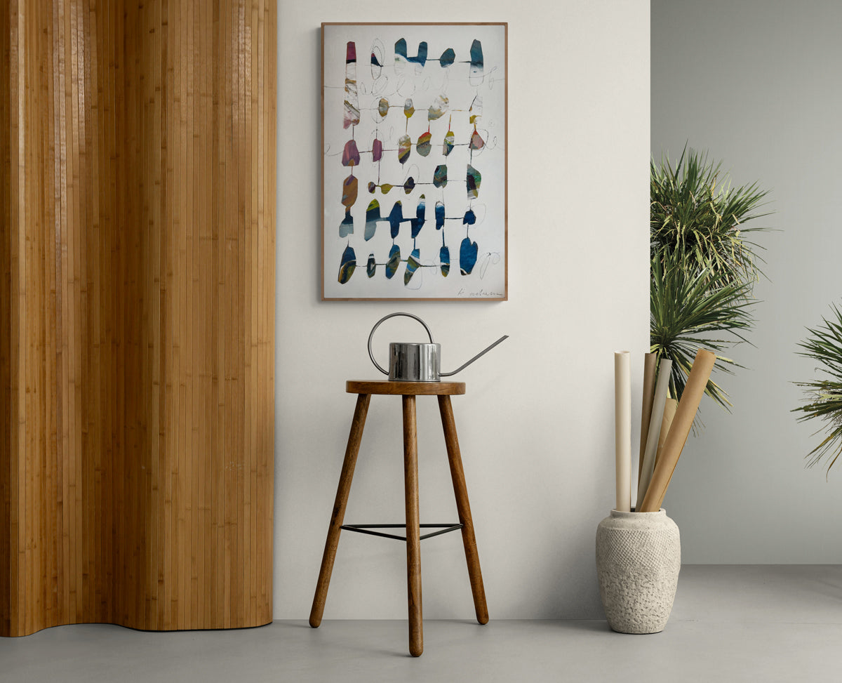 A wooden stool against a wall with a framed abstract art piece and decorative items.