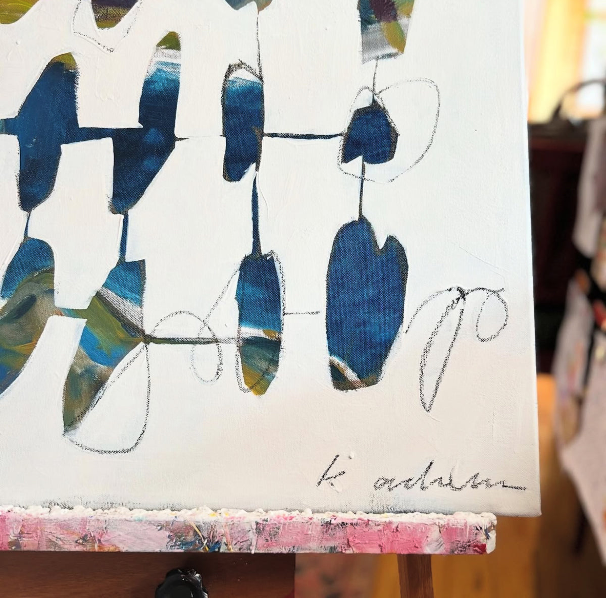 Abstract artwork with blue and green shapes on a white background resting on an easel. 