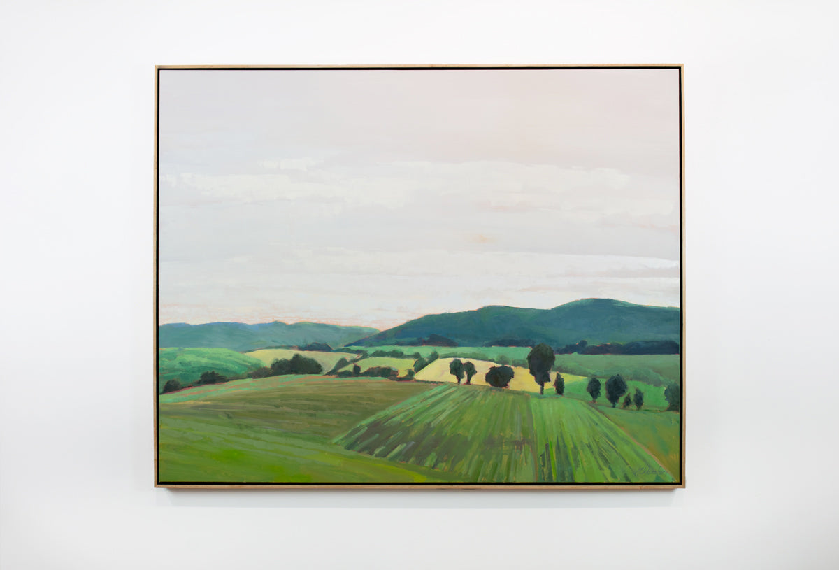 A taupe, yellow and green landscape painting by Molly Doe Wensberg hangs in a light wood floater frame on a white wall.