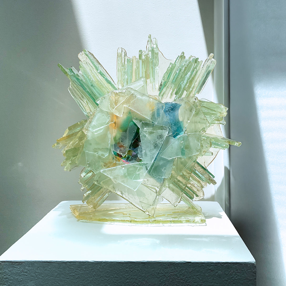 An abstract glass sculpture on a white pedestal against a neutral background. 
