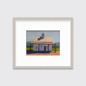 A contemporary house print in a silver frame with a mat hangs on a white wall.