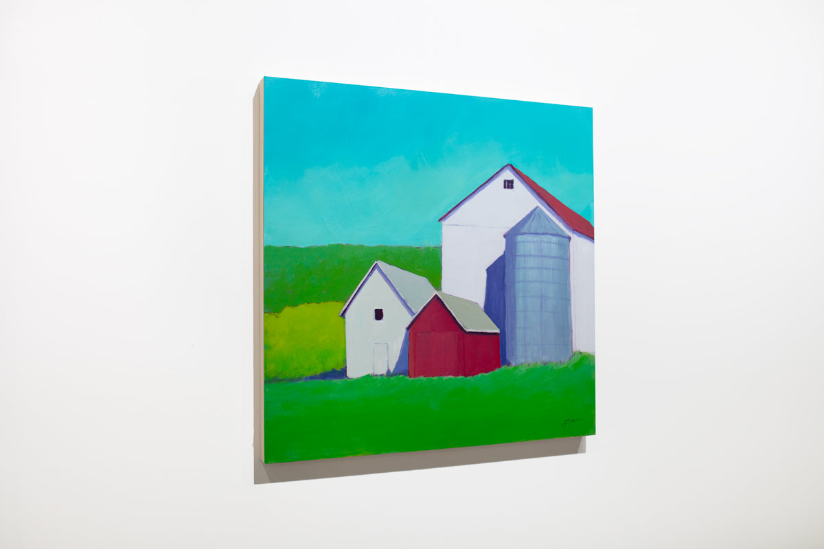 A landscape painting of white and red barns surrounded by vibrant green grass under a blue sky hangs on a white wall.