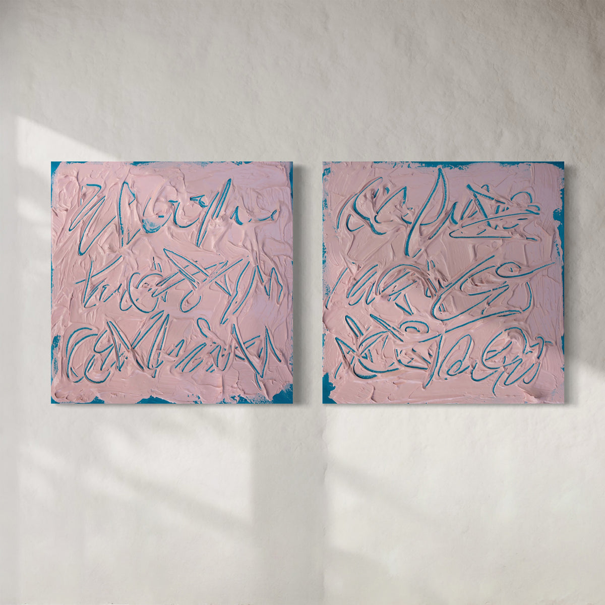 Two square abstract texted based paintings with pink backgrounds, teal textured brushstrokes, and teal line-like calligraphic forms, displayed side by side on a white wall.