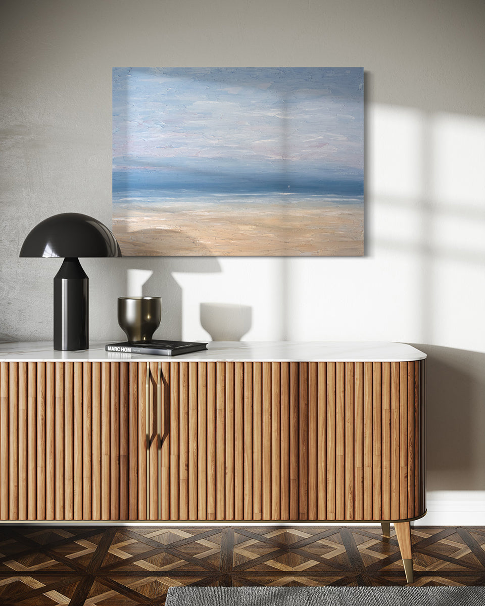 A very textured coastal painting on a white wall over a mid-century crendenza with a black lamp, dark grey ceramic bowl and a black book.