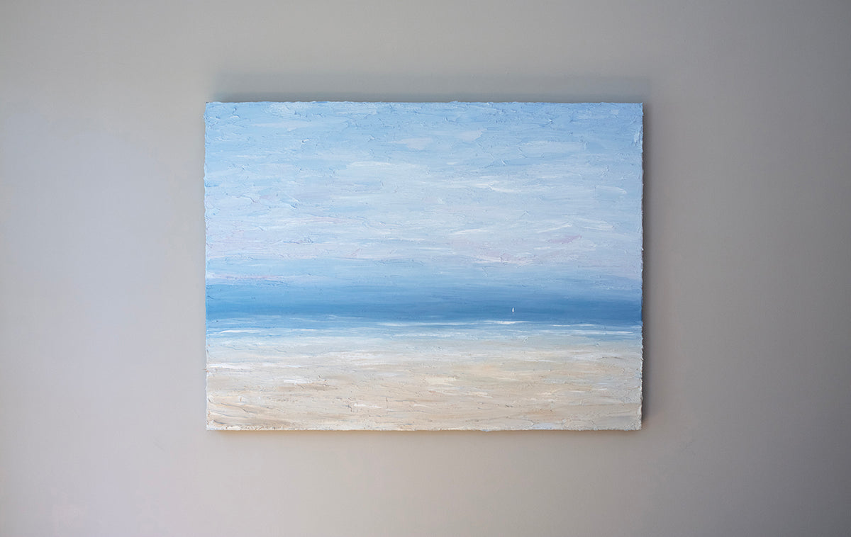 A very textured coastal painting with a lone sailboat hangs on a wall.
