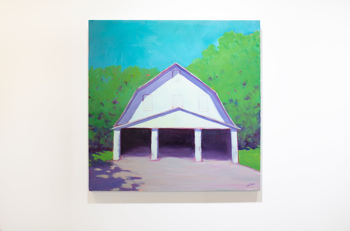A landscape painting of a white barn with three open doors, lavender shadows, blue sky and surrounded by greenery by Carol Young hangs on a white wall.