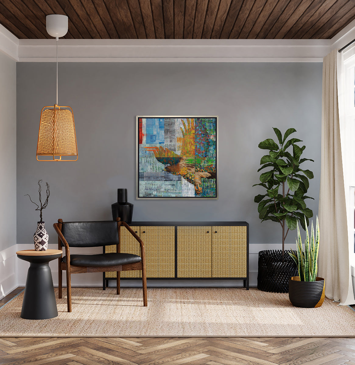 A multicolored abstract geometric print of a bald eagle in a silver floater frame hangs on a grey wall above a black and rattan cabinet with a black vase, a black leather and dark wood chair and two potted floor plants.