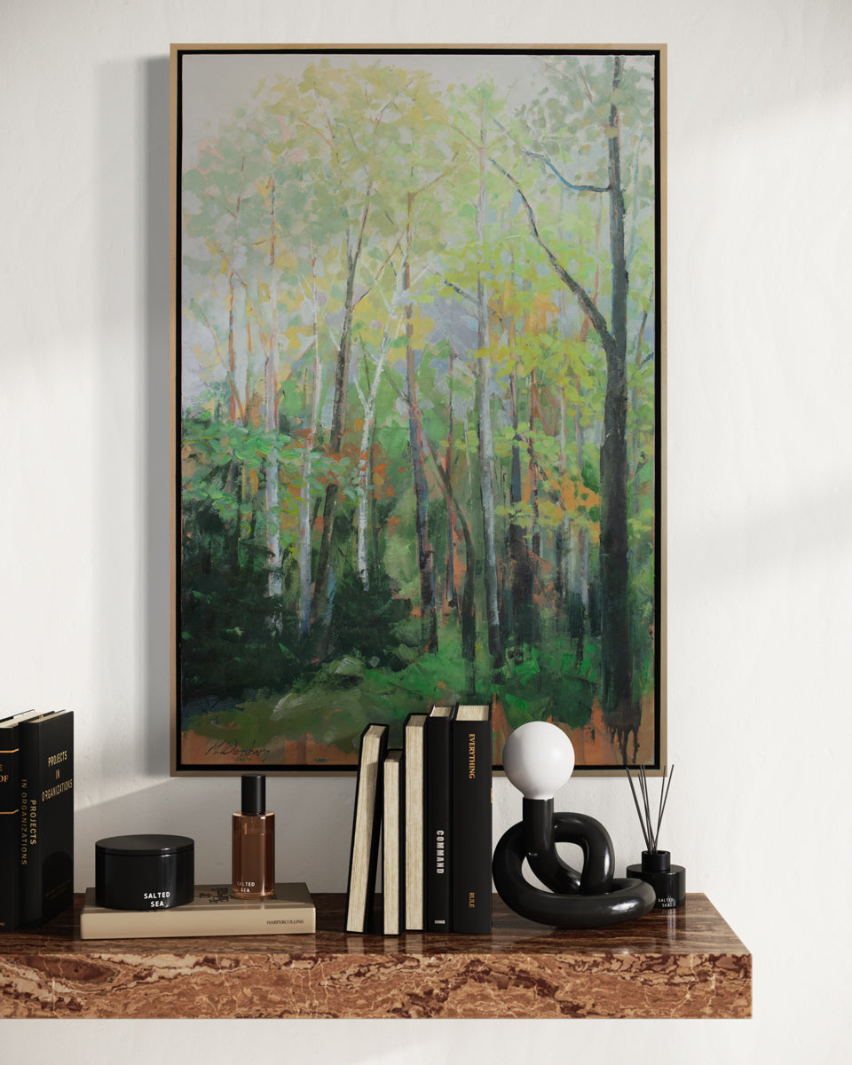 A framed green landscape painting of a forest hangs on a white wall above a floating marble shelf with black table decor.  