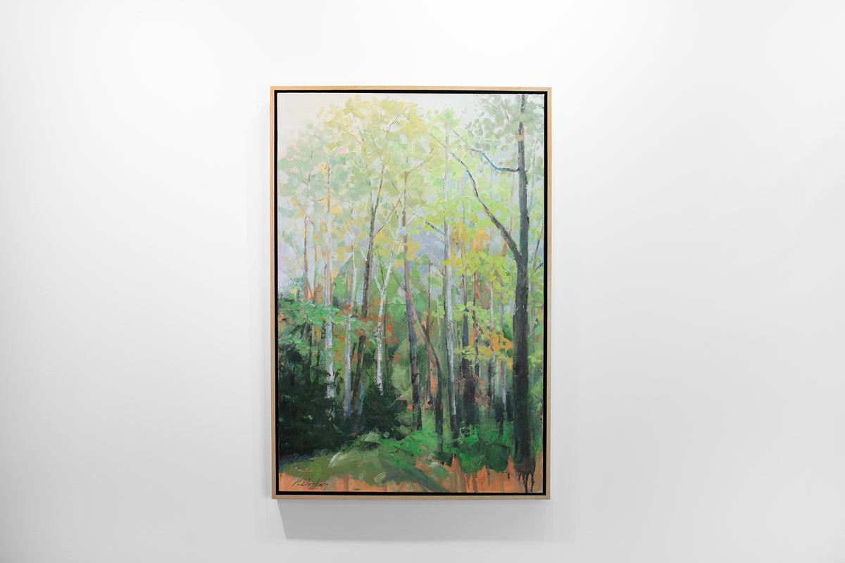 A green and orange framed painting of a forest hangs on a white wall. 