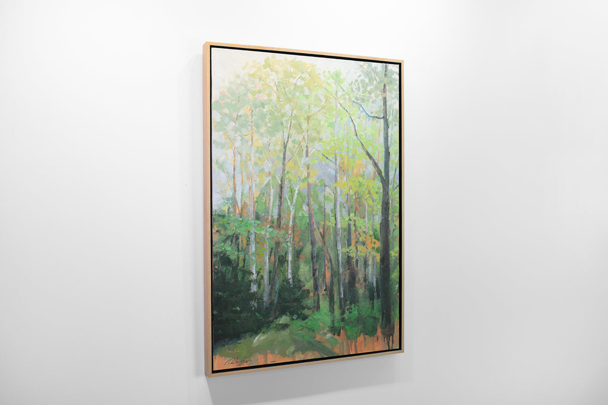 A green and orange framed painting of a forest hangs on a white wall.