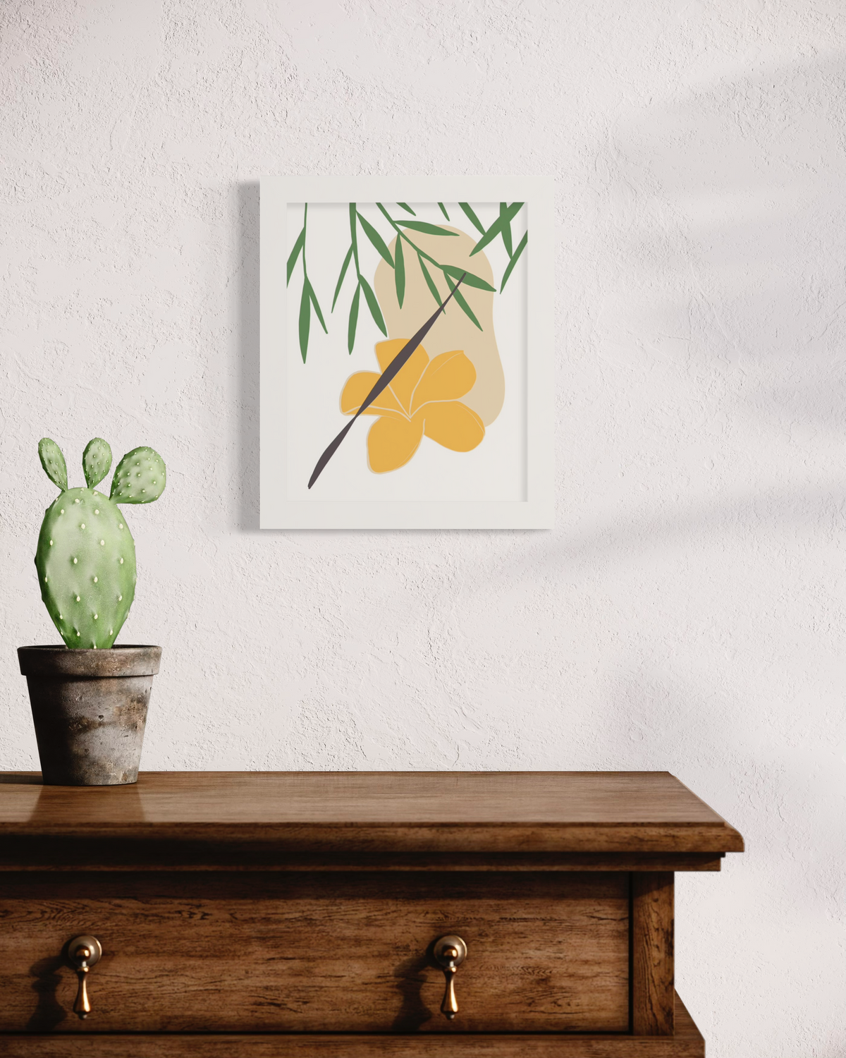 A green and yellow abstract botanical art print framed in an unmatted white frame hangs on a light wall above a wood dresser with a small potted cactus. 