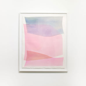 A framed pink and light blue abstract watercolor painting hangs on a white wall. 