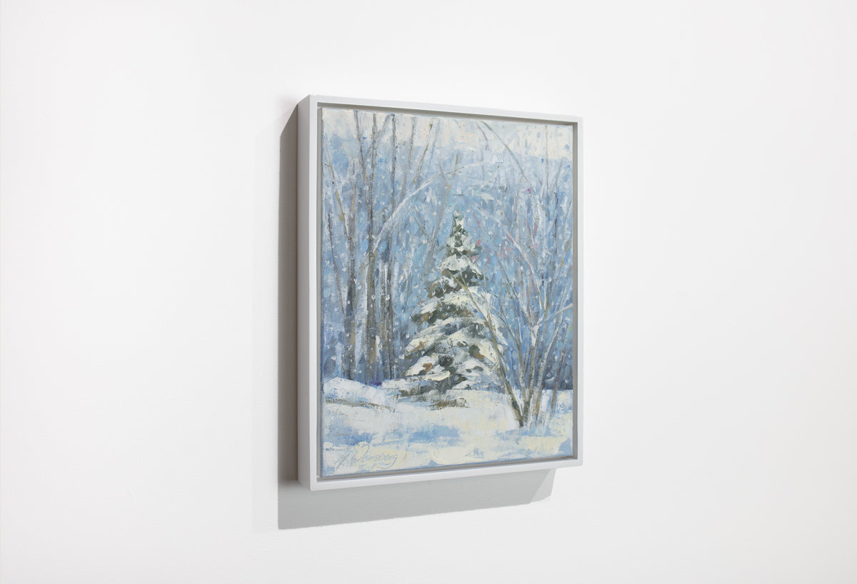 A side view of a blue, white and green snow fall landscape painting with one snow covered pine tree in the center by Molly Doe Wensberg hangs in a white floater frame on a white wall.
