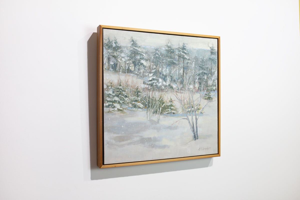 A side view of a white, grey and green snow landscape painting by Molly Doe Wensberg hangs in a light wood floater frame on a white wall.