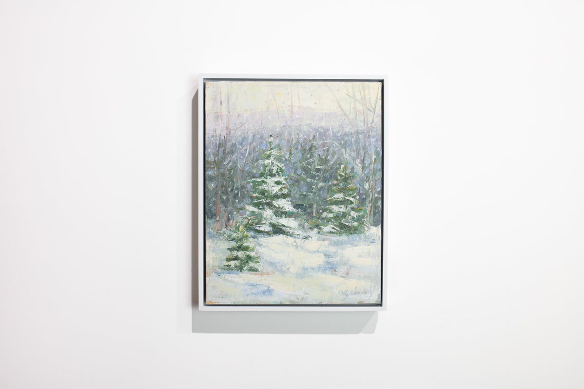 A blue, white and green snow fall landscape painting with snow covered pine trees in the center by Molly Doe Wensberg hangs in a white floater frame hangs on a white wall.