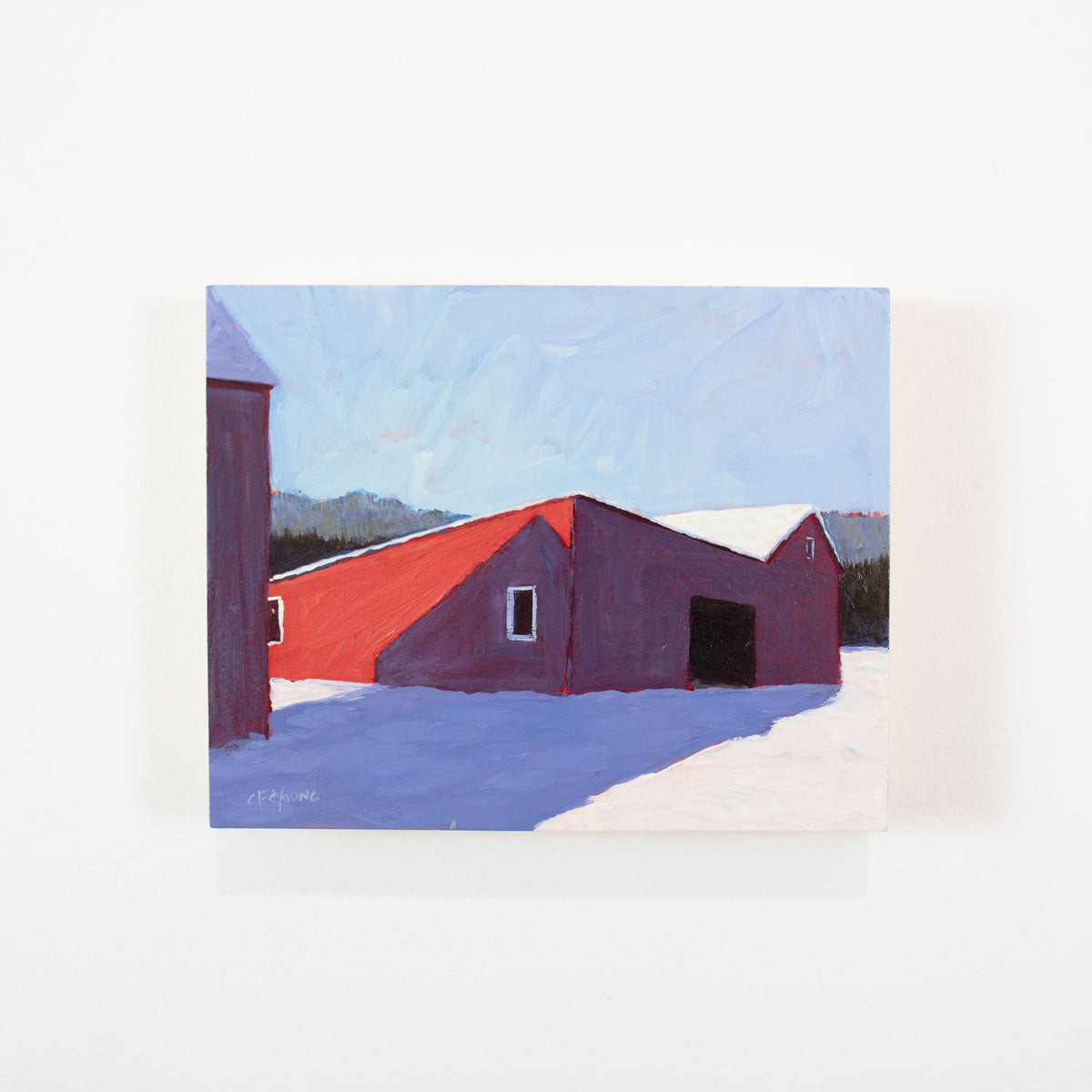 A small landscape painting of a red barn in snow hangs on a white wall. 
