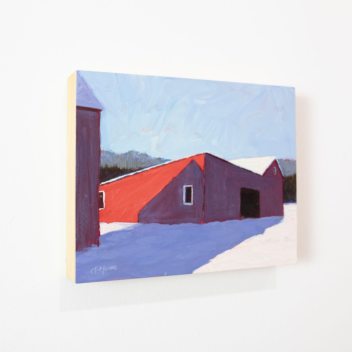 A small landscape painting of a red barn in snow hangs on a white wall.