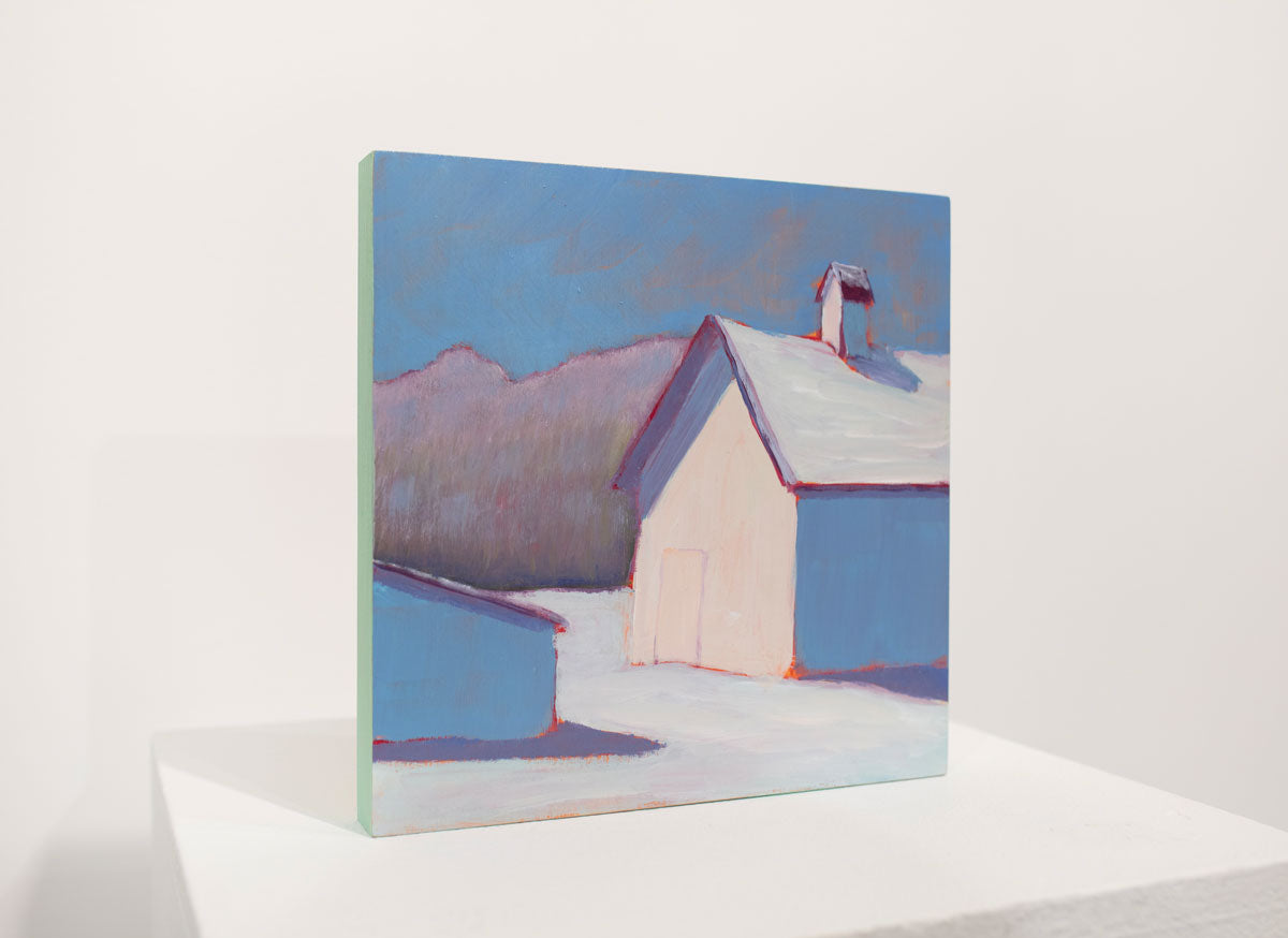 A blue, red, and white contemporary winter landscape painting stands upright on a white surface in front of a white wall.