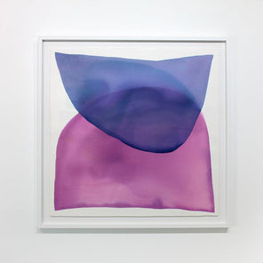 A blue and magenta minimalist abstract watercolor painting framed in a white frame hangs on a white wall.