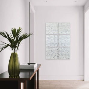  A set of six abstract paintings hang on a wall between two doors, with a dark console table in the foreground with modern table decor.
