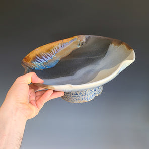 A hand holds a wide ceramic multicolored bowl. 