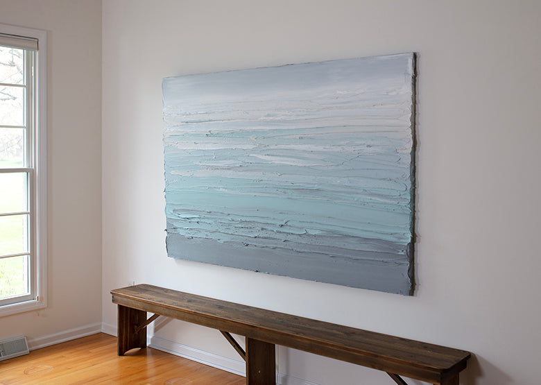 An abstract painting with turquoise impasto brushstrokes in a color gradient is seen at an angle in the artists studio.